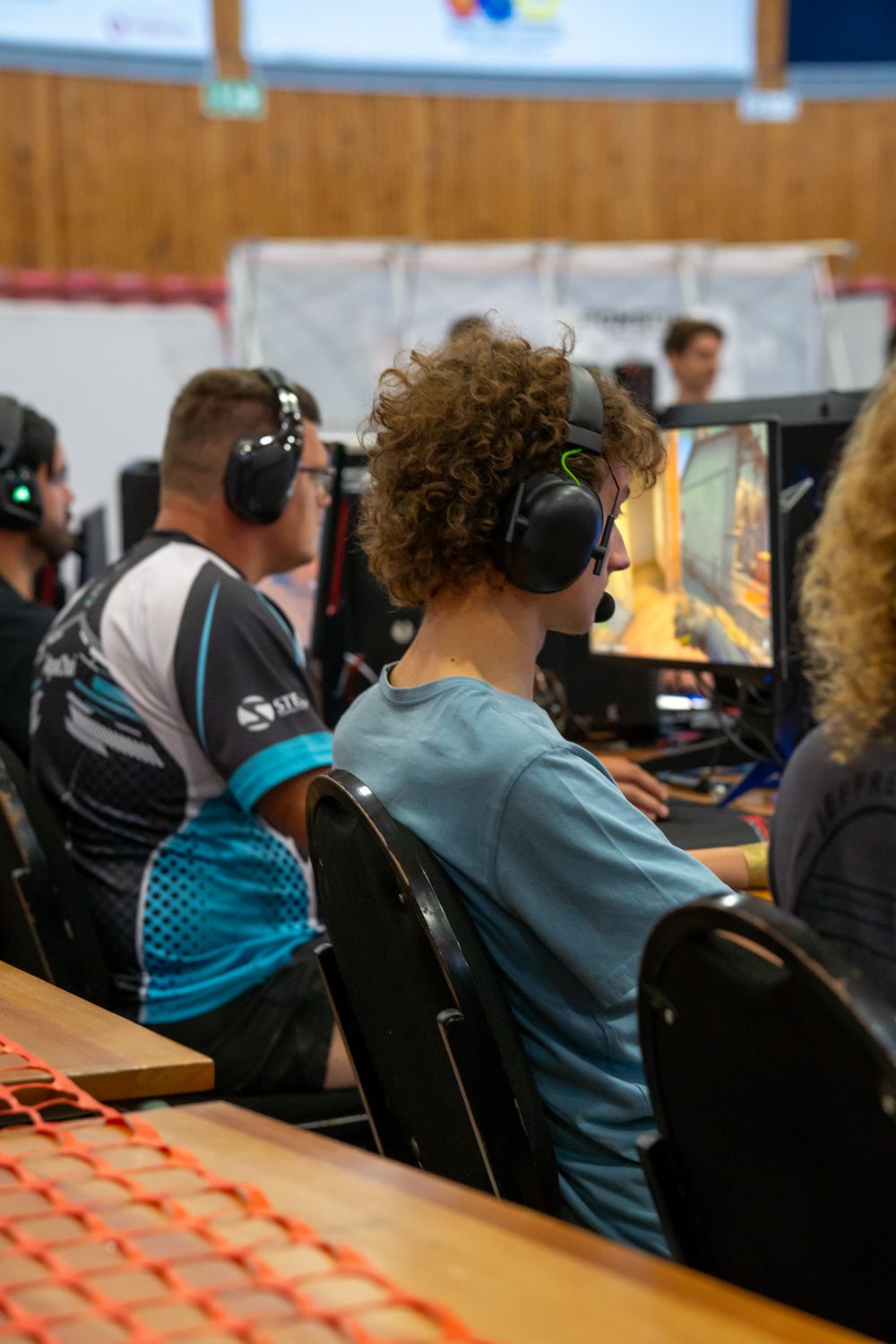 Players wearing headphones focused on video gaming at a competitive esports event indoors.