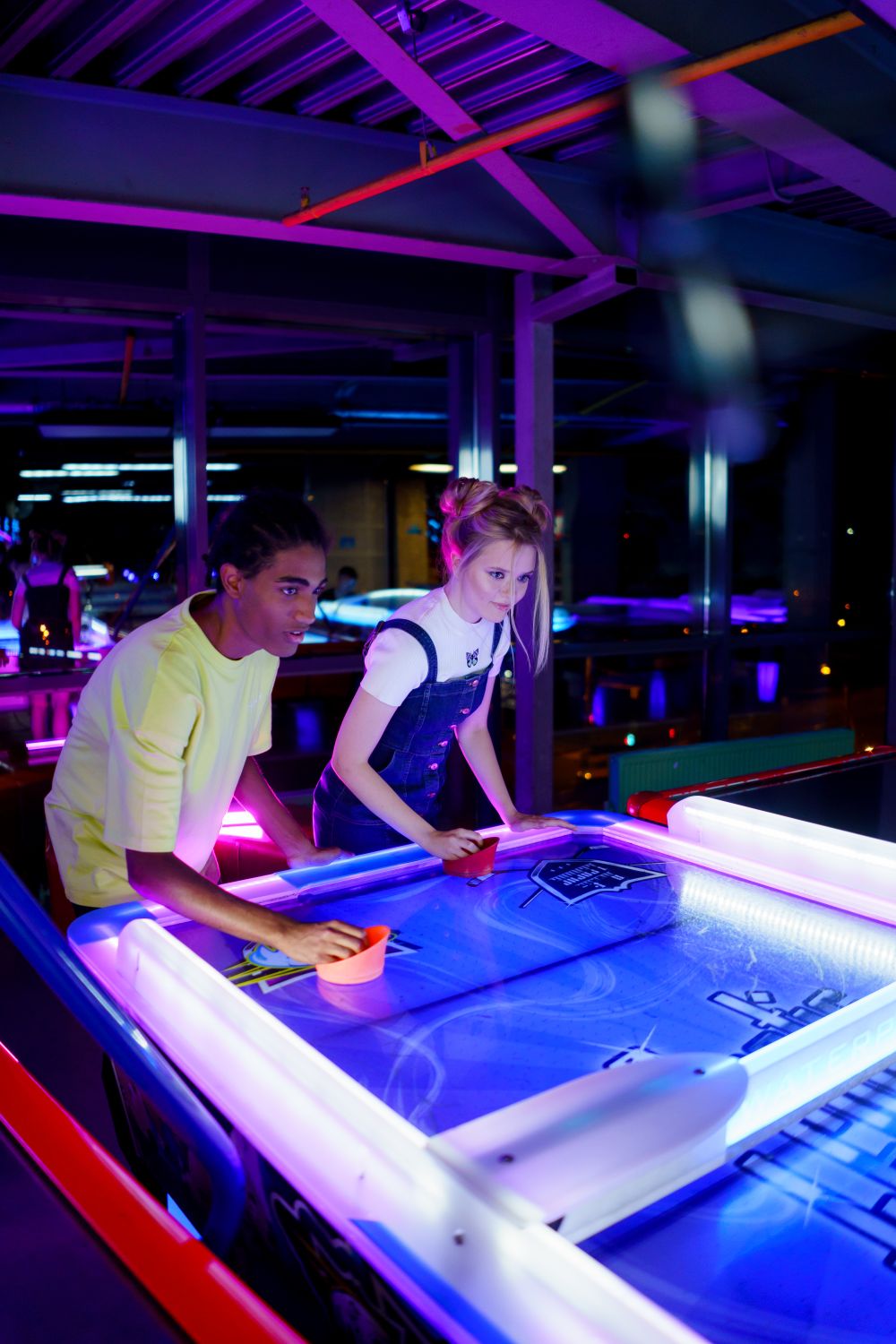 Two friends enjoying a vibrant air hockey game in a neon-lit arcade setting.