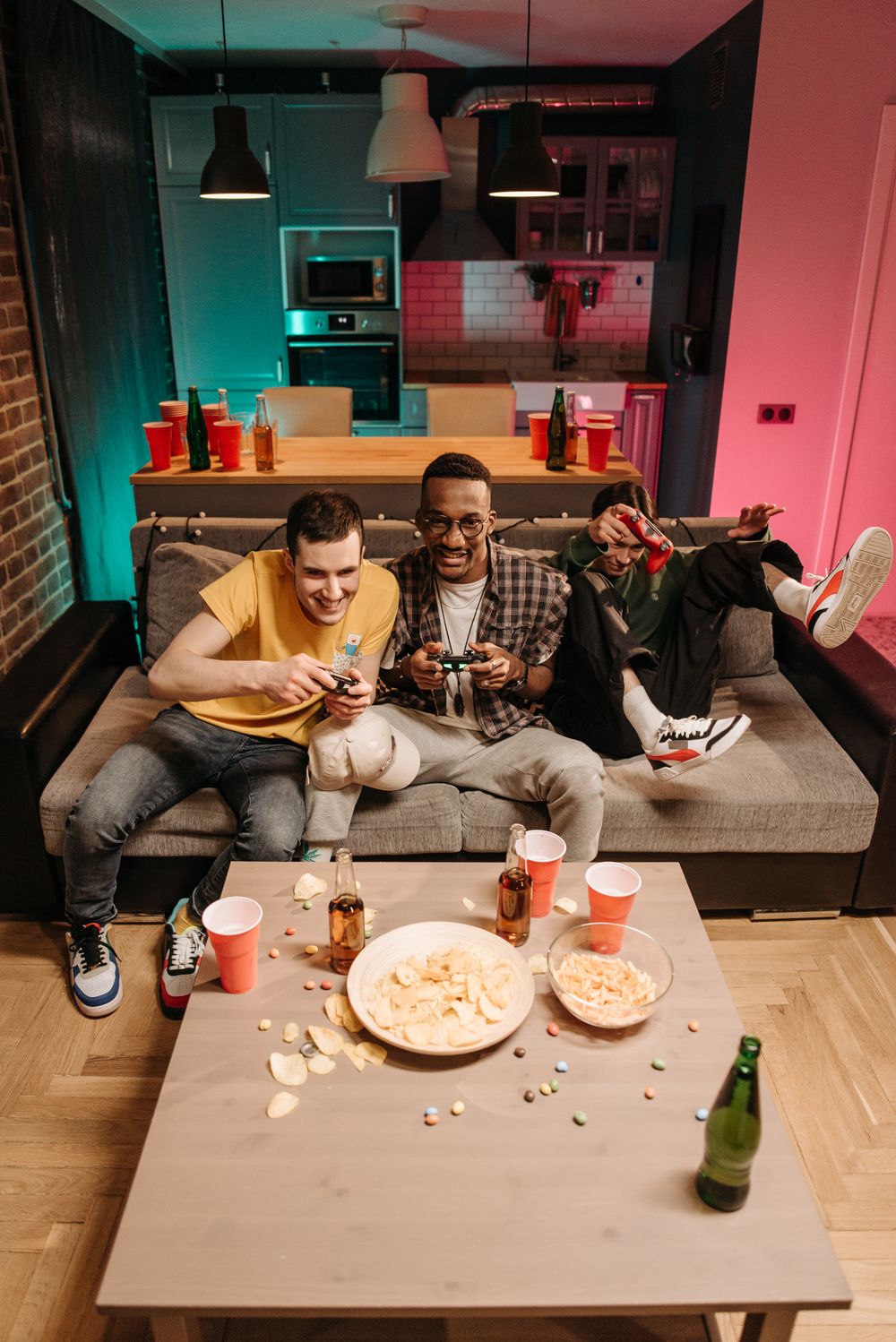 Friends enjoy video games on a couch with snacks and drinks, creating a lively living room scene.
