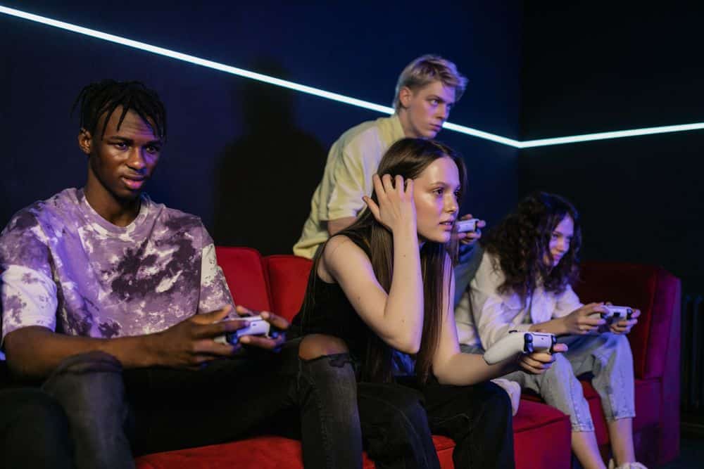 Group of friends enjoying a gaming session on a red sofa with wireless controllers.