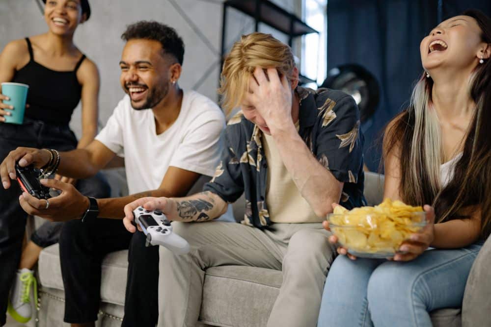 Diverse group of friends having fun playing video games indoors, sharing laughter and snacks.