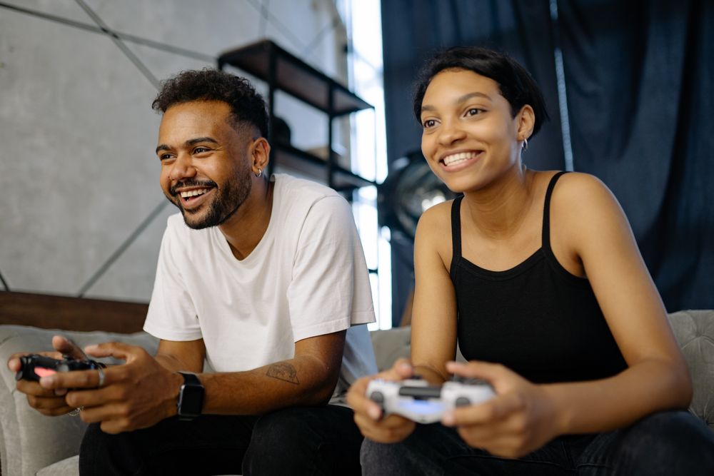 A couple playing video games on a sofa, engaged and smiling indoors.