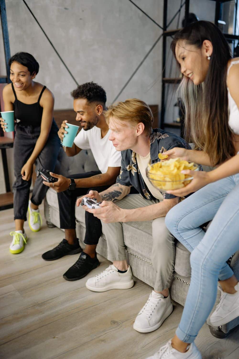 A group of diverse friends playing video games indoors, happily gathered around a sofa.