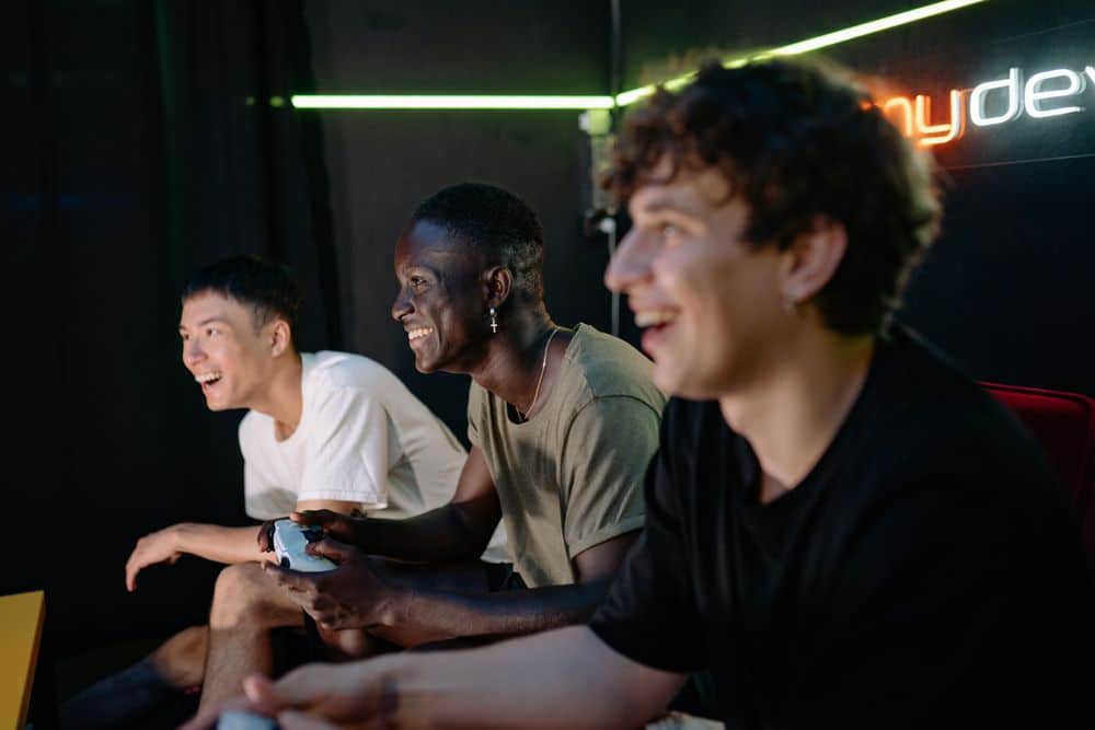 Three diverse young men playing video games indoors, showing excitement and enjoyment.